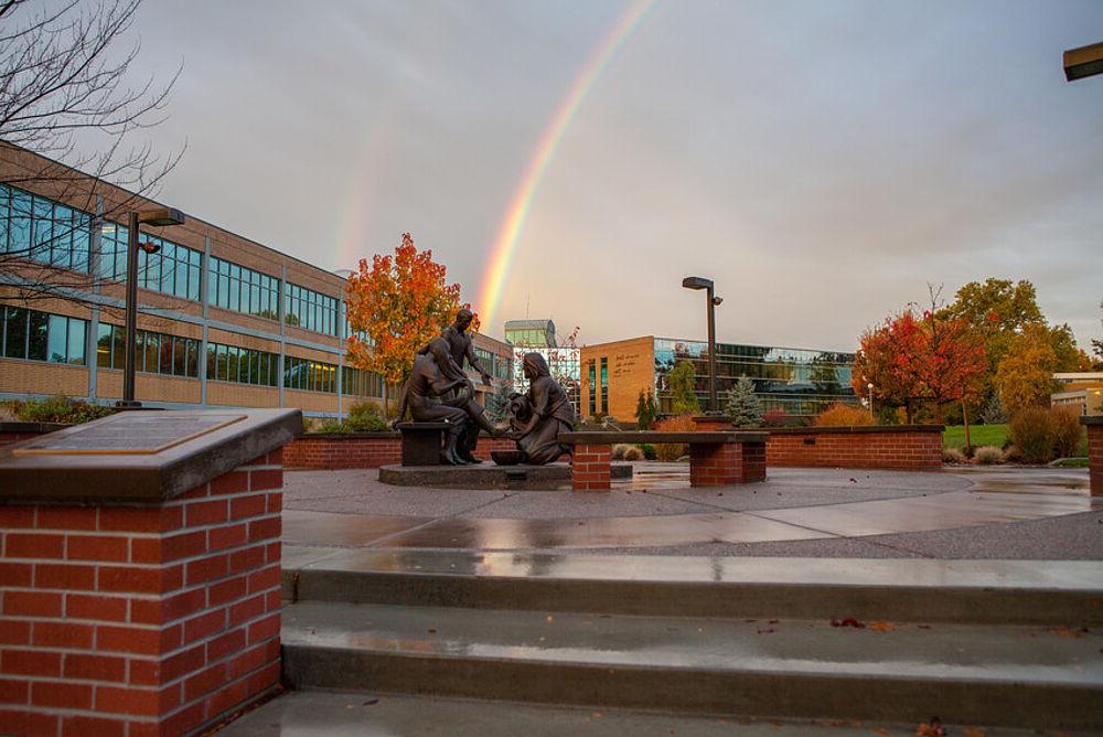 一场暴风雨过后，校园树上的落叶，天空中出现了彩虹，前景是耶稣雕像.